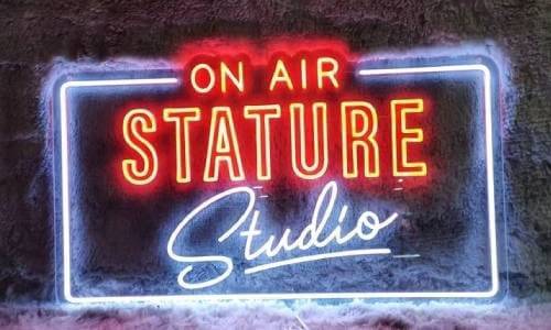 A neon sign with the text 'ON AIR STATURE' in bold orange, and 'Studio' in white cursive.