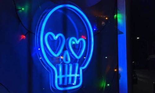A bright blue neon sign of a skull with heart-shaped eyes.